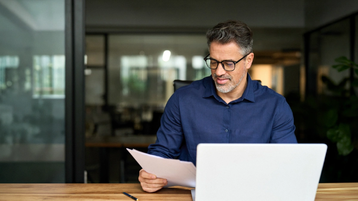 Man med glasögon och kort grått skägg bakom laptopskärm.
